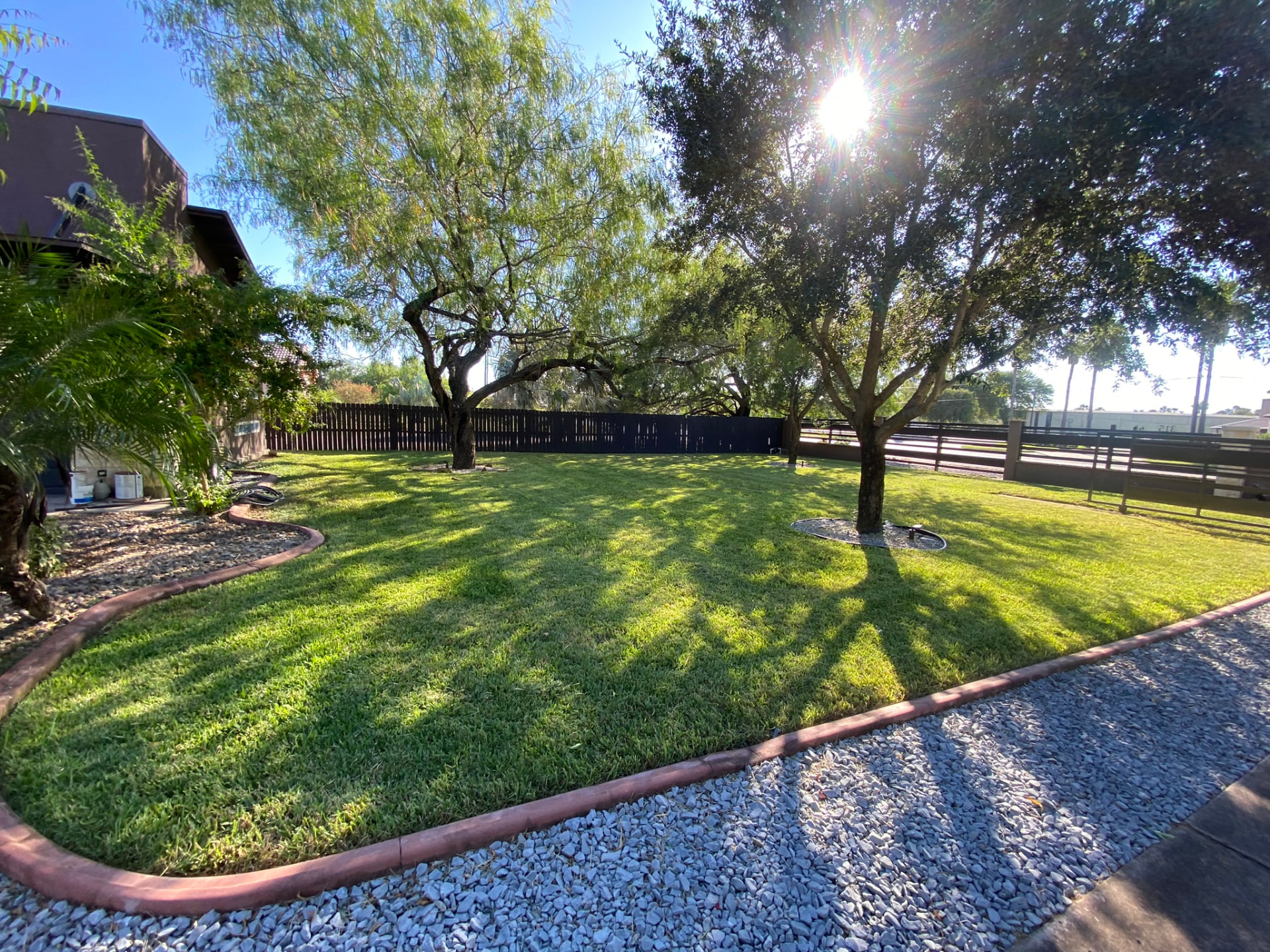 Freshly mowed backyard lawn with shade trees, stone border and privacy fence in south Texas